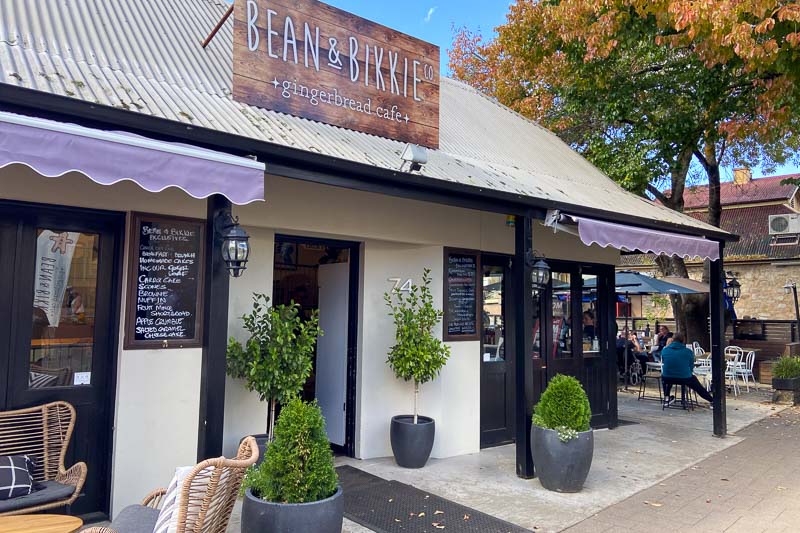 Exterior of Bean & Bikkie gingerbread cafe with a rustic design, outdoor seating, and a chalkboard menu by the entrance.