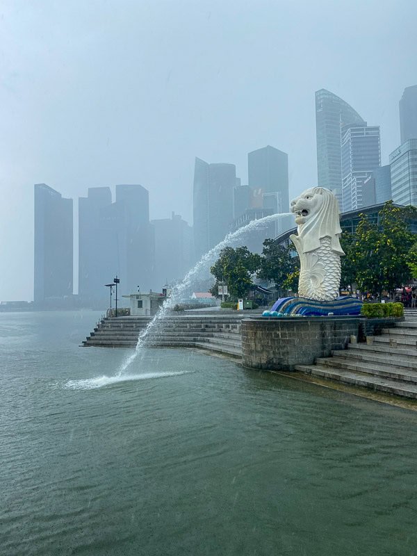 Merlion statue spouting water into Marina Bay with misty skyscrapers in the background.