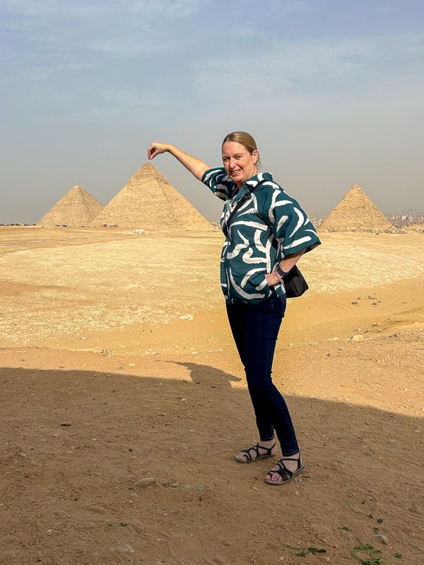 What I Packed - 8 weeks, Hot & Cold 5 Person posing with an arm extended, appearing to touch the tip of a pyramid in the background, with two other pyramids visible under a clear sky.