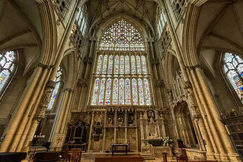 European Churches Worth Visiting 5 Interior of a large Gothic cathedral featuring tall stone arches, ornate stained glass windows, and religious artwork above the altar.