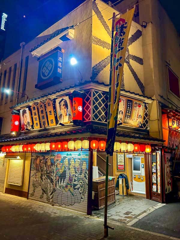 Tokyo Free Walking Tours: 3 Tours I Tried and Recommend 7 A Japanese restaurant with bright lanterns, colorful banners, and posters of performers on the exterior, photographed at night.