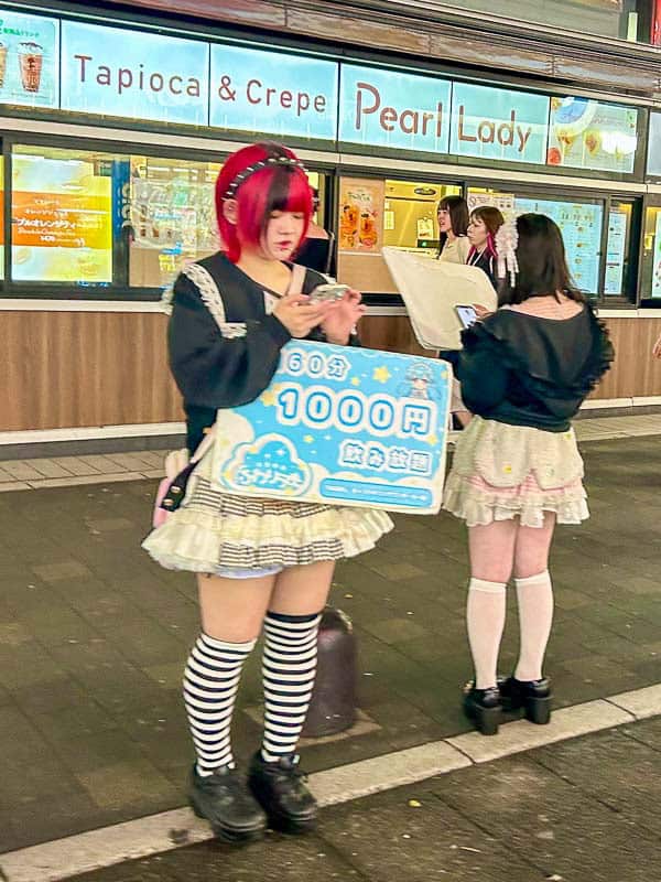 Tokyo Free Walking Tours: 3 Tours I Tried and Recommend 21 Two women in matching outfits stand outside a shop; one holds a sign advertising a 60-minute 1000 yen offer, with a menu for "Pearl Lady" tapioca and crepe visible in the background.