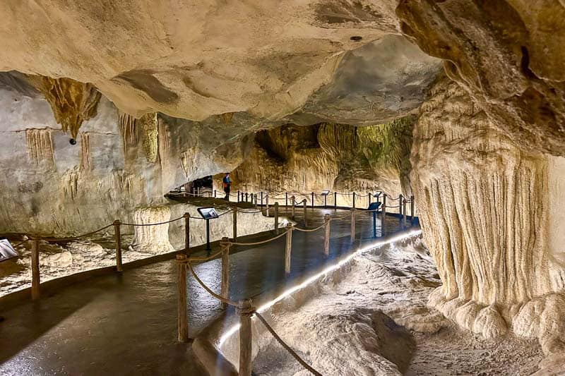 Which Mandai Wildlife Park Should You Visit? I Tried All Five 37 A paved walkway with rope railings winds through a cave with textured rock formations and stalactites, illuminated by lights along the path.