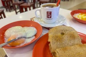 Where to Eat Kaya Toast in Singapore: 9 Places I've Tried 36 A breakfast set with two soft-boiled eggs, toast, and a cup of coffee on a white table, served on red plates in a casual dining setting.
