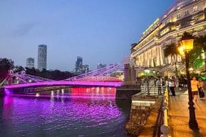 Weekend in Singapore: Itinerary for Repeat Visitors 28 Evening view of a brightly lit bridge with pink lights over a river, modern skyscrapers in the background, and people walking near a large historic hotel—perfect for a vibrant weekend in Singapore.