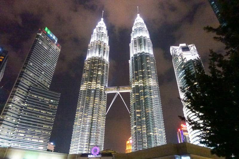 The Petronas Twin Towers in Kuala Lumpur illuminated at night, with surrounding high-rise buildings and a cloudy sky—an iconic highlight of any Singapore & Malaysia Itinerary.