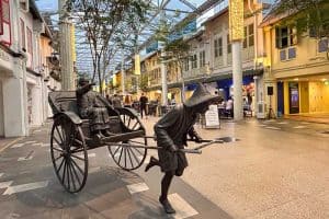 Best Areas to Stay in Singapore 25 Bronze sculpture of a rickshaw puller and passenger in an open-air shopping street with cafes and traditional-style buildings.