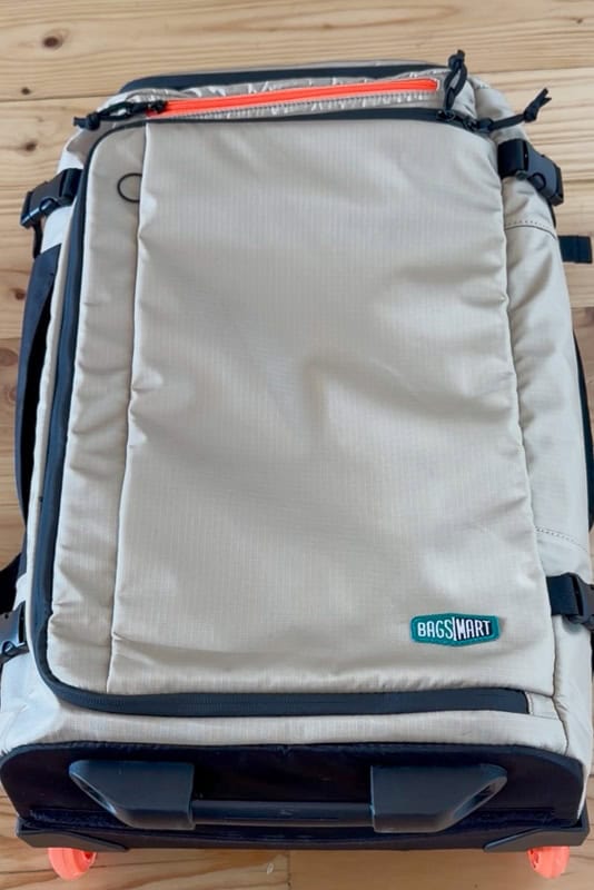 BAGSMART BLAST Series Review: Tested on My Travels 12 A light beige BAGSINART Blast 40L Rucksack lies flat on a wooden surface. The bag features black and orange accents, with visible zips and handles. The brand logo is on the lower right corner.