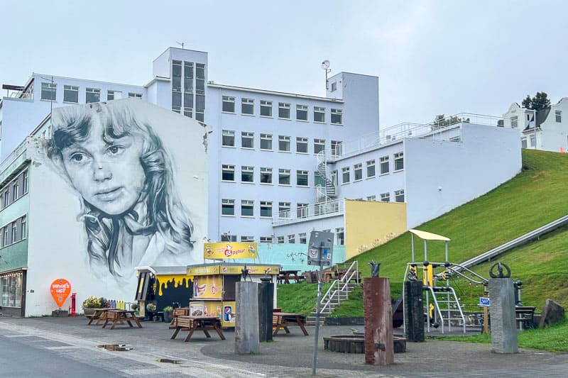 10 Days in Iceland: Our Real Itinerary 38 Large building with a mural of a woman's face, playground equipment, picnic tables, and a small yellow food stand—perfect for sharing stories from your 10 days in Iceland over lunch.