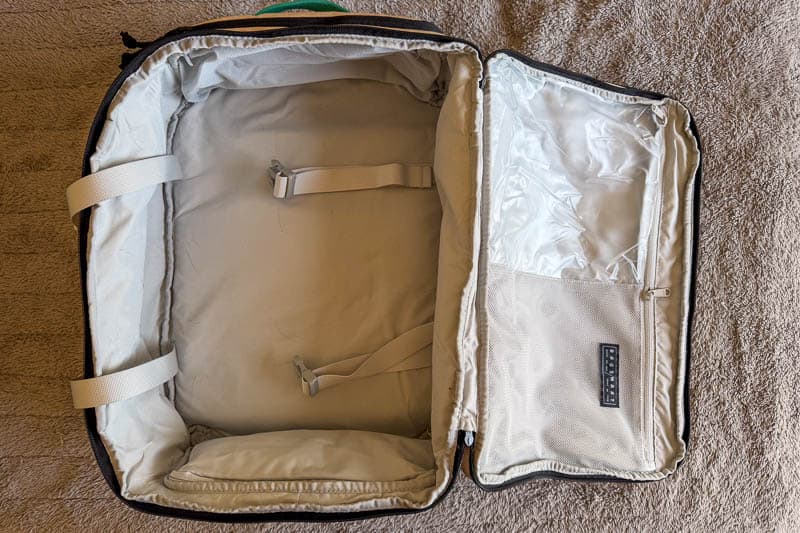 BAGSMART BLAST Series Review: Tested on My Travels 3 Open, empty suitcase with light-coloured lining, interior tie-down straps, and a mesh zippered pocket on the lid, resting on a textured beige surface—perfectly complementing your Blast 40L Rucksack for organised travel.