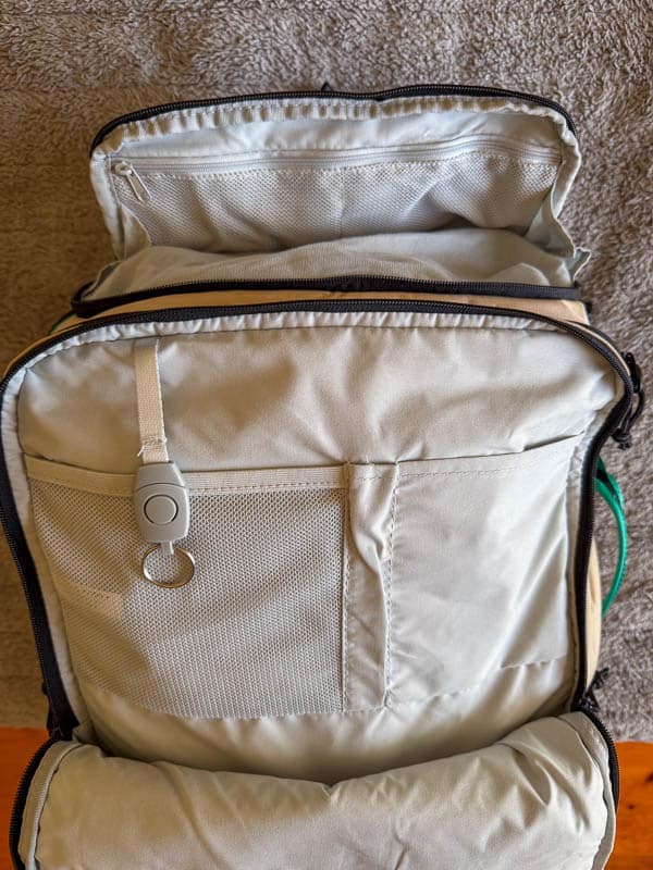 BAGSMART BLAST Series Review: Tested on My Travels 6 A beige Blast 40L Rucksack with its main compartment unzipped, revealing mesh and fabric pockets inside, a key ring attachment, and a zip-fastened pocket on the top flap. The rucksack rests on a textured surface.