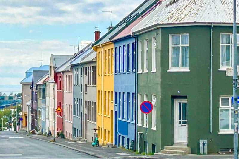 Guesthouse Aurora Review - Our One-Night Stay in Reykjavik 9 A row of colourful houses, including green, blue, yellow, and pink, lines a sloped street. A no parking sign is visible, and the sky is partly cloudy.