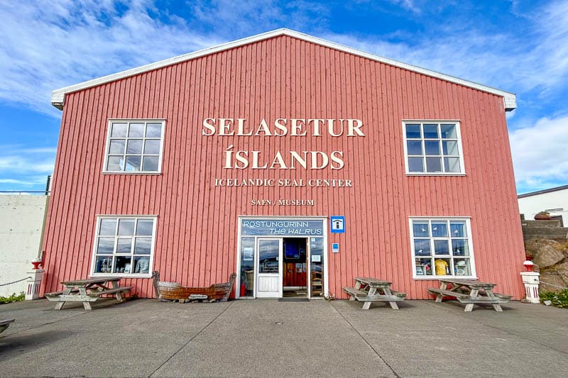 10 Days in Iceland: Our Real Itinerary 41 A large red wooden building houses the Icelandic Seal Center, a must-visit stop during 10 days in Iceland, with benches outside and a sign reading “Selasetur Íslands” on the front.