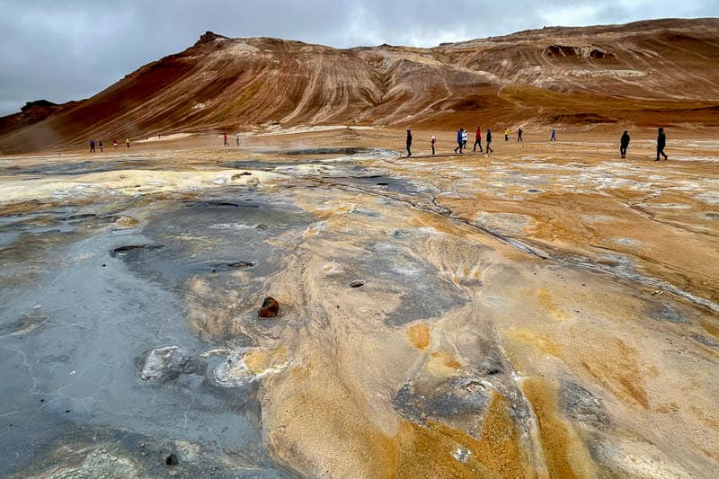 People explore a barren, rocky landscape with ochre and brown hills under a cloudy sky, capturing the rugged beauty of 10 days in Iceland.