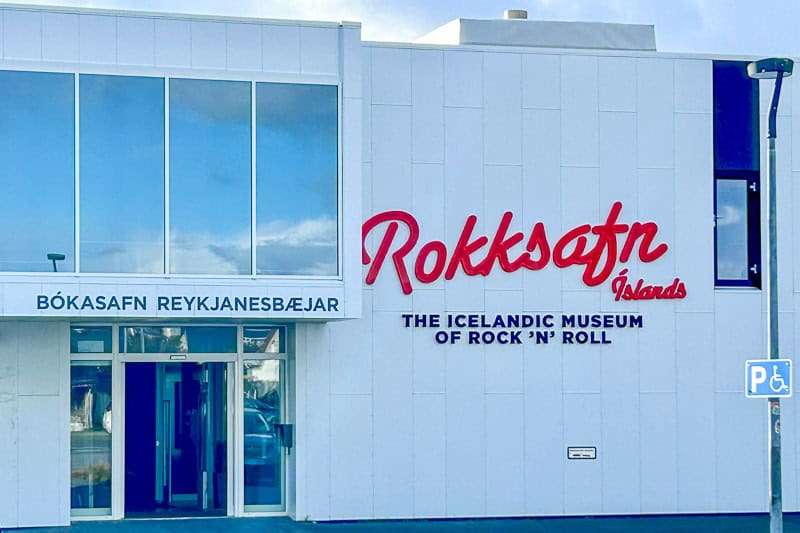 Kef Guesthouse Review - A Handy Overnight Stay Near Keflavík Airport 7 The exterior of the Icelandic Museum of Rock 'n' Roll, near Kef guesthouse, features large red and black signage in Icelandic and English on a white building, with a blue disabled parking sign out front.