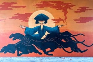 Street Art in Iceland 42 A mural depicts a person in a blue robe and large hat, holding a smoking pipe, sitting among the silhouettes of several black panthers against an orange background with red clouds and a large yellow sun.