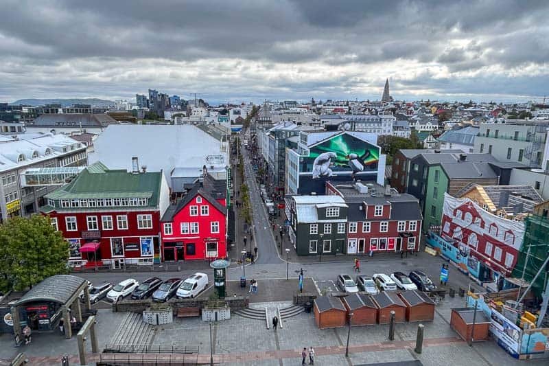 Things I Wish I Had Done in Iceland 2 An aerial view of a city street lined with colorful buildings, reminiscent of sights from 10 days in Iceland, with people walking below and a cloudy sky overhead.