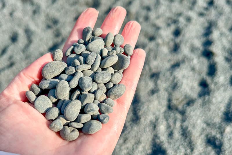 10 Days in Iceland: Our Real Itinerary 19 A hand holding a collection of small, smooth grey pebbles with a sandy surface in the background—capturing a quiet moment from 10 days in Iceland.