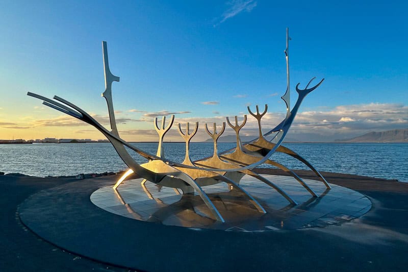 10 Days in Iceland: Our Real Itinerary 3 A large, metallic, abstract sculpture resembling a Viking ship stands by the waterfront with the sea and distant mountains in the background—a must-see during your 10 days in Iceland.