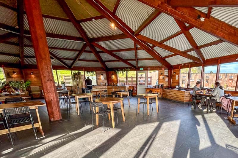 Iceland Campgrounds 6 Spacious wooden restaurant interior with large windows, exposed beams, and scattered tables; a few people are seated near the windows.