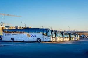 How to Get From Keflavík Airport to Reykjavík 38 A row of parked Flybus coaches is lined up in a car park under clear blue skies, with some urban buildings and construction cranes visible in the background.