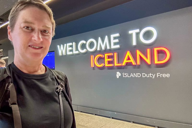 Budget Tips for Iceland 5 A person taking a selfie in front of a wall sign that reads "WELCOME TO ICELAND" and "ISLAND Duty Free" inside what appears to be an airport terminal.