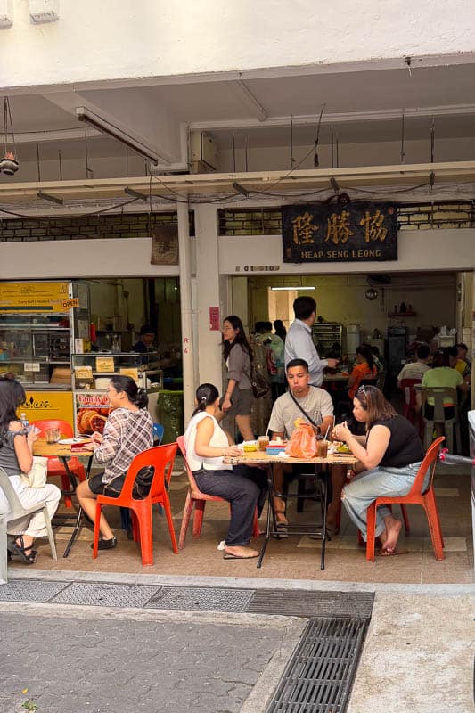 Where to Eat Kaya Toast in Singapore: 9 Places I've Tried 14 People are seated at plastic tables and chairs outside a small eatery with a sign reading “Heap Seng Leong.” Some are eating and talking, while others are ordering food at the counter. The scene is casual and lively.