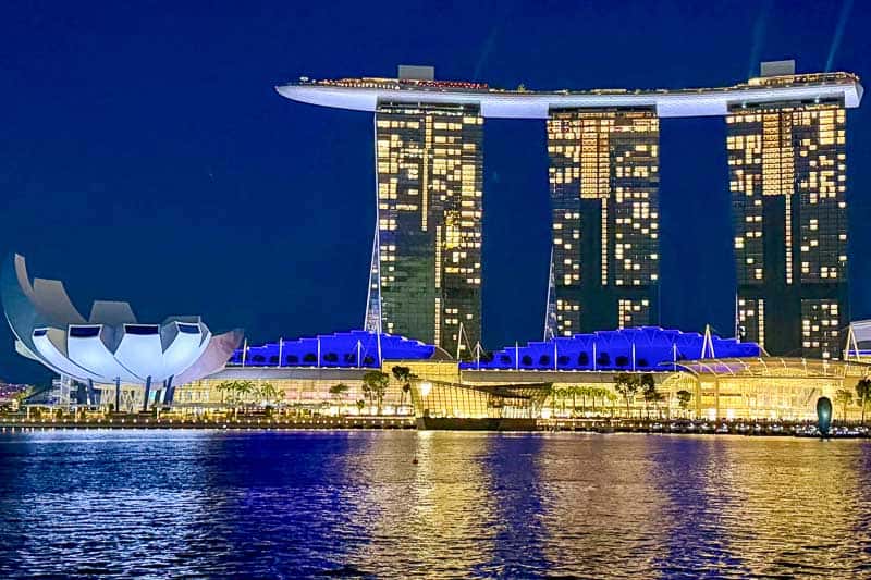 32 Fun Things to do in Singapore on a Budget 3 Night view of Marina Bay Sands hotel with three towers and a boat-shaped rooftop in Singapore, brightly lit with reflections on the water; the ArtScience Museum is visible on the left.