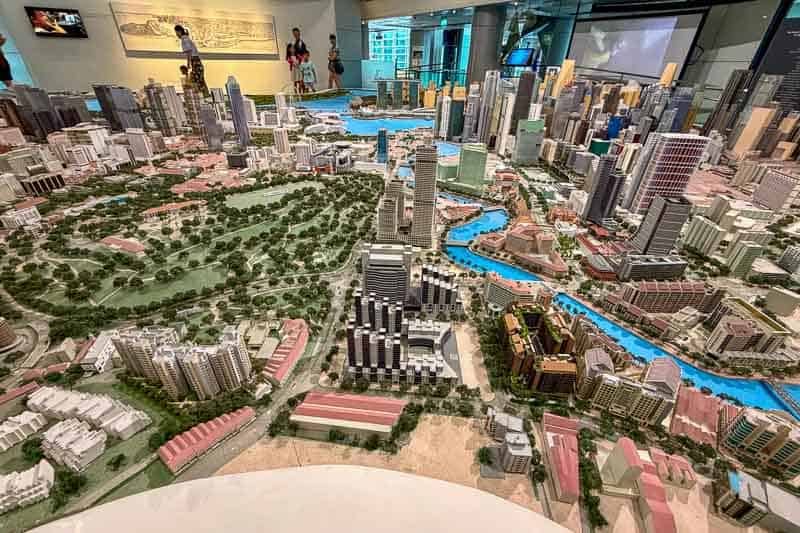 32 Fun Things to do in Singapore on a Budget 7 A detailed scale model of a city with high-rise buildings, green parks, and a winding river is displayed indoors at the Singapore City Gallery. Several people observe the model in the background.